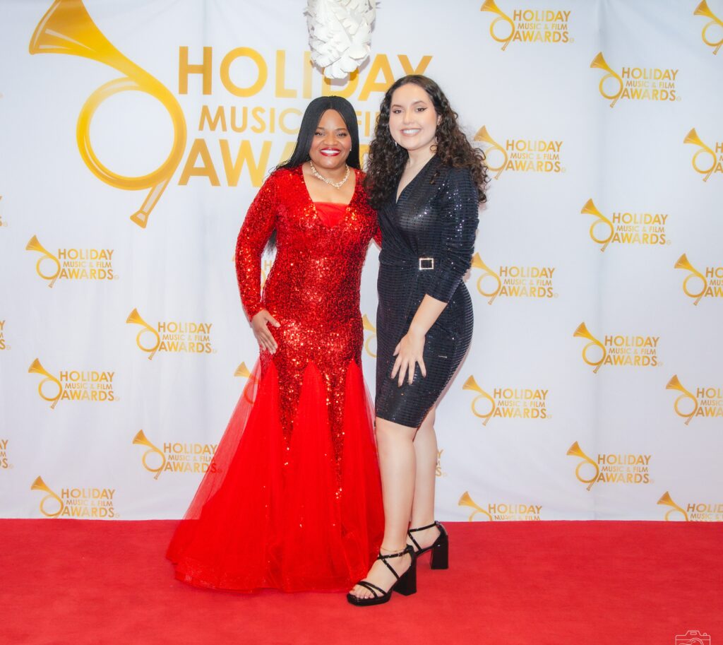 Two women in red dress standing on a red carpet.