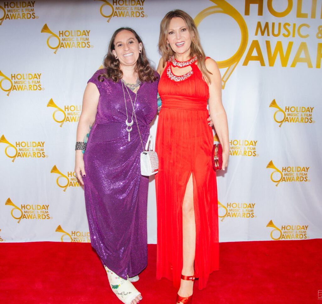 Two women in red and purple dresses on a red carpet.