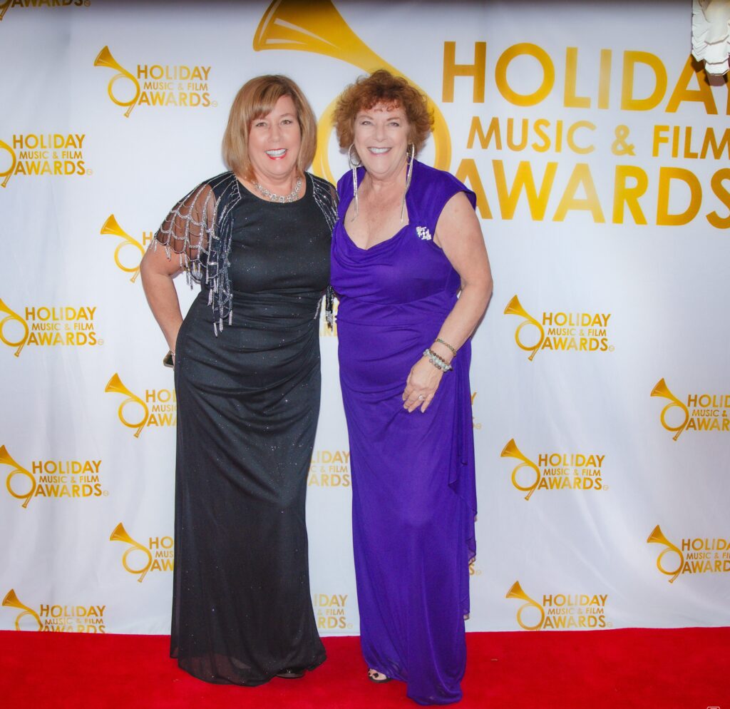 Two women in black and purple dresses on a red carpet.