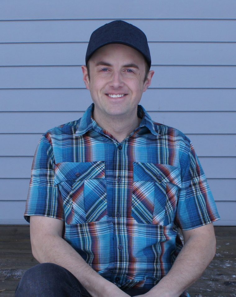 A man sitting on the ground wearing a blue plaid shirt.